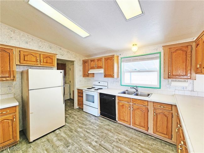 Kitchen with light wood finished floors, a sink, under cabinet range hood, white appliances, and lofted ceiling | Image 8