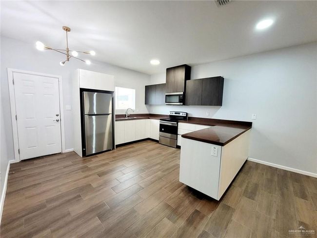 Kitchen featuring an inviting chandelier, a peninsula, dark wood-style floors, dark countertops, and appliances with stainless steel finishes | Image 5