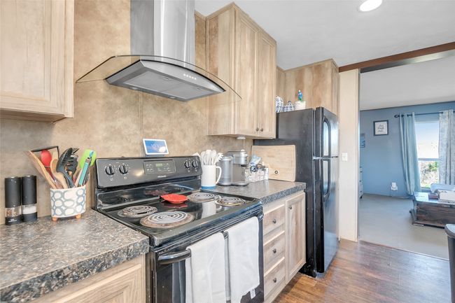 Kitchen featuring dark countertops, wall chimney range hood, light brown cabinetry, wood finished floors, and electric range | Image 21