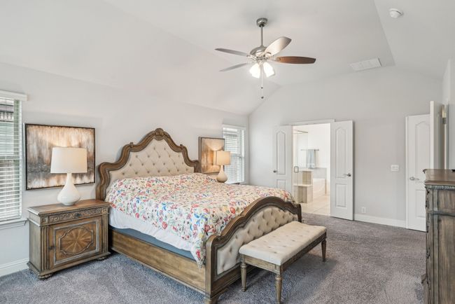 Carpeted bedroom featuring vaulted ceiling, lots of windows for added lights, connected bathroom, and ceiling fan | Image 24