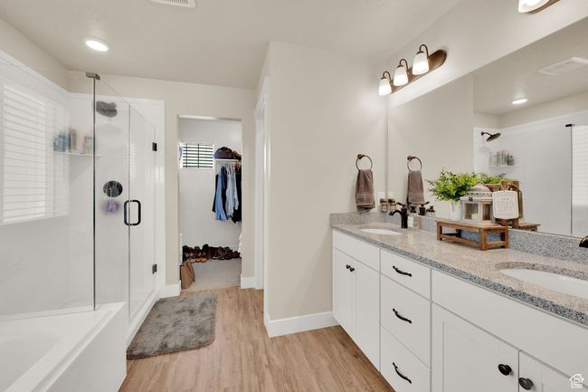 Bathroom featuring a stall shower, double vanity, wood finished floors, a spacious closet, and a bath | Image 22