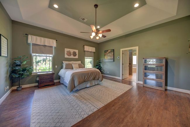 Spacious Primary Bedroom features a tray ceiling with recessed lighting, ceiling fan, and includes large windows for natural light. The room leads to an en-suite bathroom, enhancing convenience and privacy. | Image 15