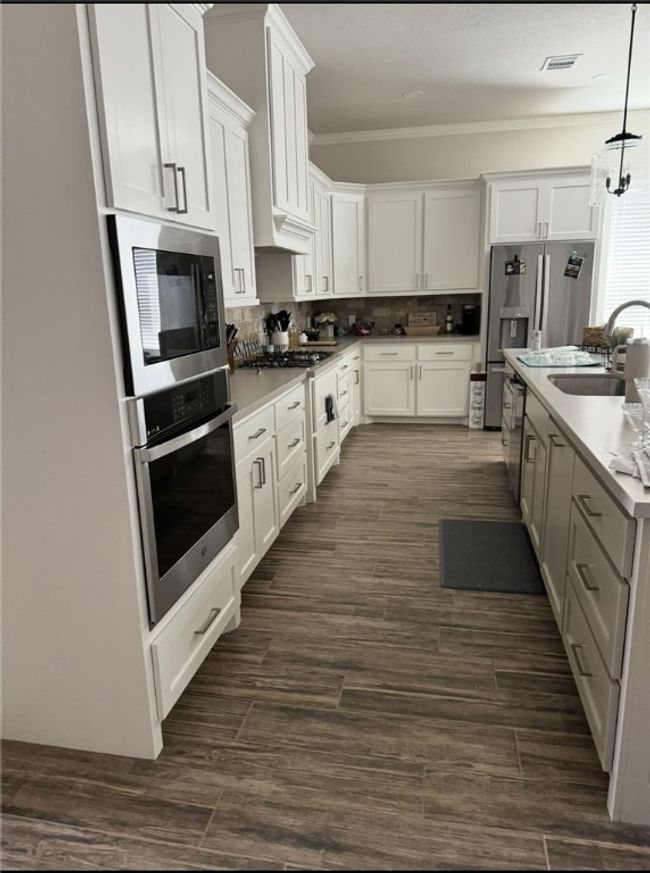 Kitchen with appliances with stainless steel finishes, backsplash, white cabinetry, decorative light fixtures, and crown molding | Image 10