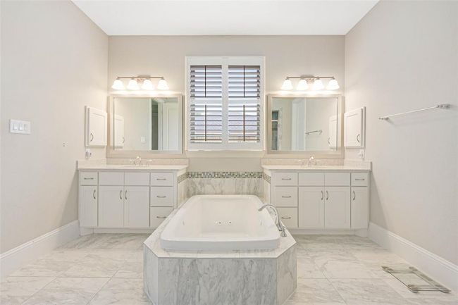 Elegant primary bath featuring double vanities, a central jetted soaking tub with marble surround, and spacious tile flooring. | Image 26