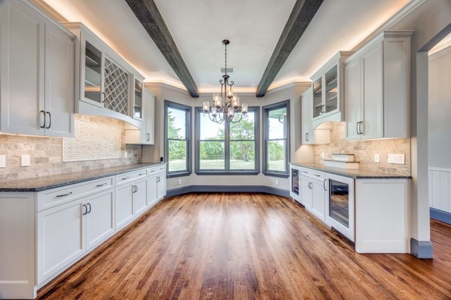 Kitchen featuring wine cooler, a chandelier, wood finished floors, dark stone counters, and beam ceiling | Image 7