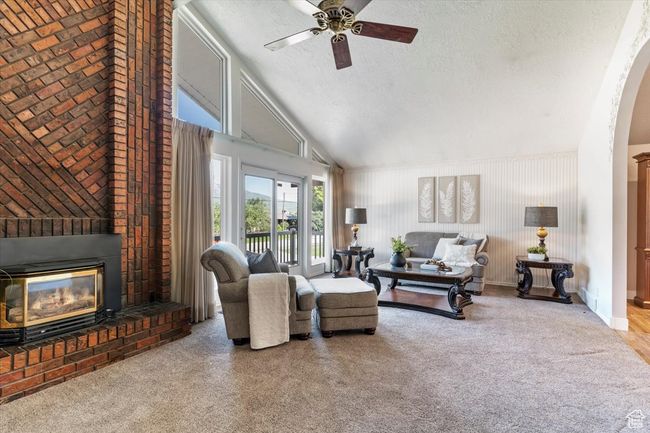 Carpeted living area featuring a ceiling fan, a textured ceiling, a brick fireplace, vaulted ceiling, and arched walkways | Image 8