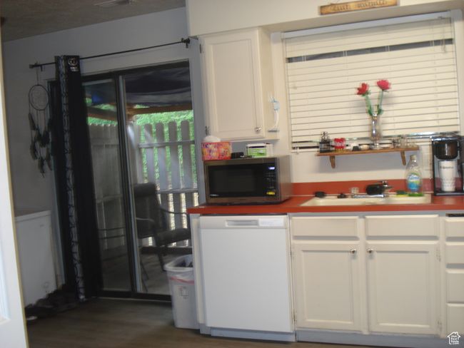 Kitchen with stainless steel microwave, white dishwasher, white cabinets, and dark wood-style floors | Image 23