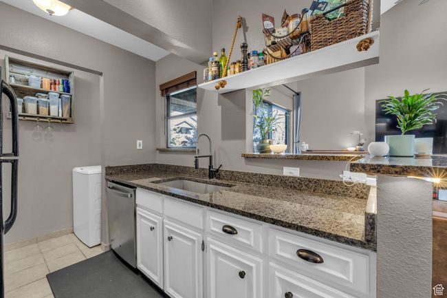 Kitchen featuring dark stone countertops, dishwasher, a sink, white cabinetry, and light tile patterned flooring | Image 7