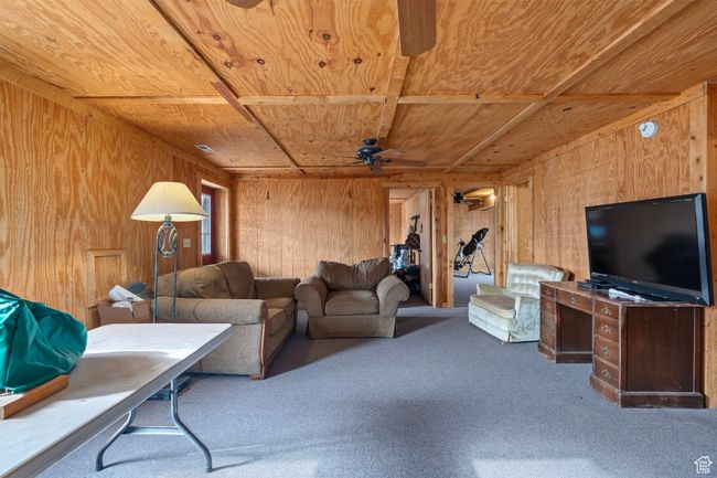 Carpeted living room featuring ceiling fan, wood walls, and wooden ceiling | Image 7