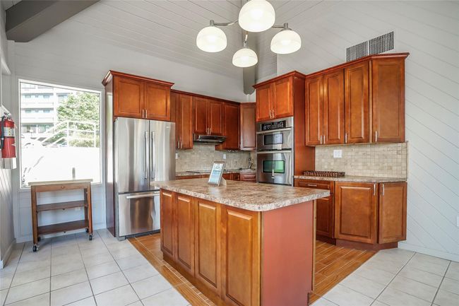 Kitchen in club house featuring light tile patterned flooring, appliances with stainless steel finishes, a kitchen island, hanging light fixtures, and vaulted ceiling | Image 37