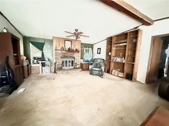 Spacious living room with a cozy stone fireplace, built-in wooden bookshelves, and ceiling fan. Bright with natural light, perfect for relaxation and gatherings. | Image 4