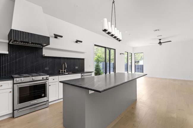 Kitchen with stainless steel appliances, dark countertops, white cabinets, a center island, and light wood-style floors | Image 8