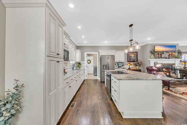 Kitchen featuring a sink, appliances with stainless steel finishes, a lit fireplace, ornamental molding, and light stone counters | Image 11