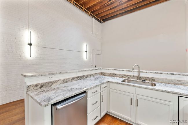 Kitchen featuring stainless steel dishwasher, light wood-type flooring, white cabinets, light stone countertops, and brick wall | Image 4