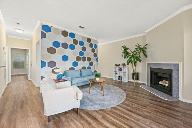 Living room with crown molding, wood finished floors, baseboards, and a tile fireplace | Image 6
