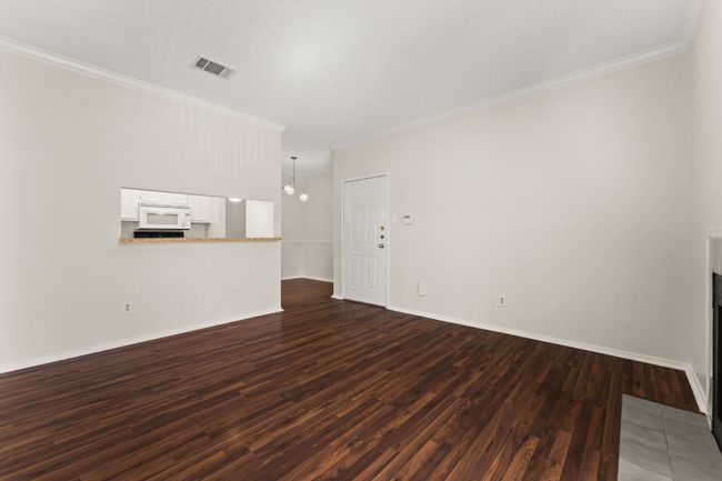 Unfurnished living room with crown molding, dark wood-style floors, visible vents, and baseboards | Image 7