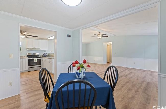 Dining space featuring a ceiling fan, a wainscoted wall, light wood finished floors, crown molding, and vaulted ceiling | Image 14