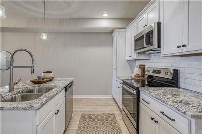 Kitchen featuring appliances with stainless steel finishes, backsplash, sink, pendant lighting, and white cabinets | Image 3