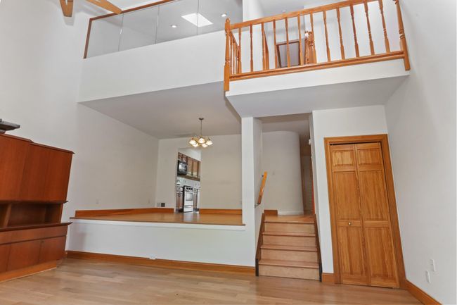 Unfurnished living room featuring a towering ceiling, stairs, wood finished floors, a chandelier, and baseboards | Image 21