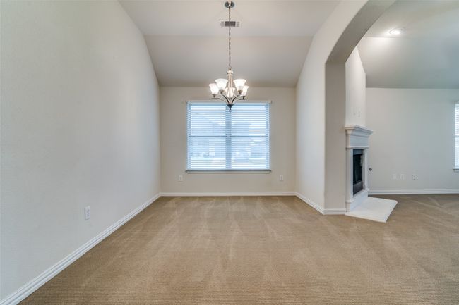 Unfurnished dining area with carpet, a chandelier, arched walkways, vaulted ceiling, and a fireplace with raised hearth | Image 6