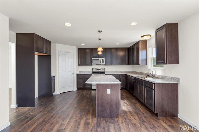 Kitchen with stainless steel appliances, dark brown cabinets, dark wood finished floors, light countertops, and a center island | Image 7