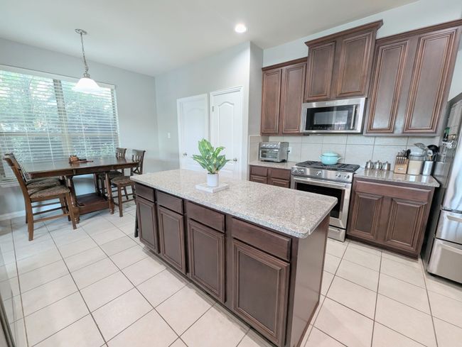 Kitchen featuring appliances with stainless steel finishes, decorative backsplash, hanging light fixtures, light tile patterned floors, and dark brown cabinets | Image 24