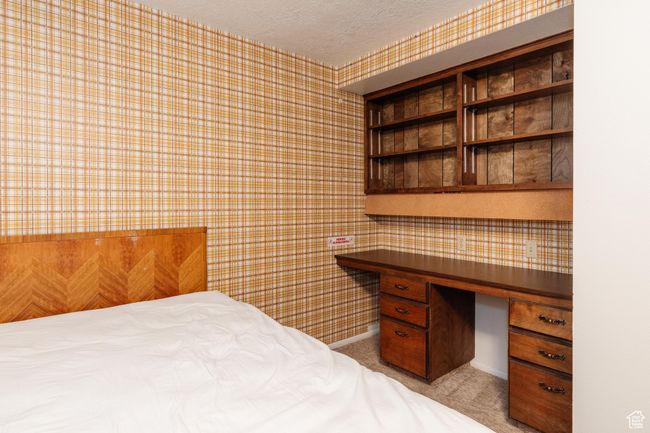 Bedroom featuring wallpapered walls, a textured ceiling, light carpet, and built in desk | Image 25