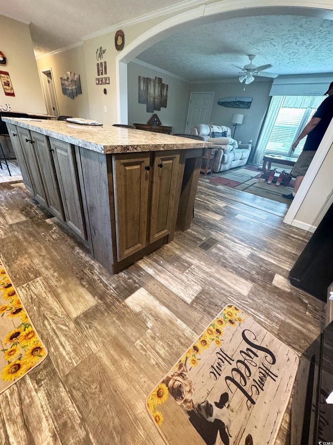 Kitchen with a textured ceiling, ceiling fan, arched walkways, a kitchen island, and wood finished floors | Image 15