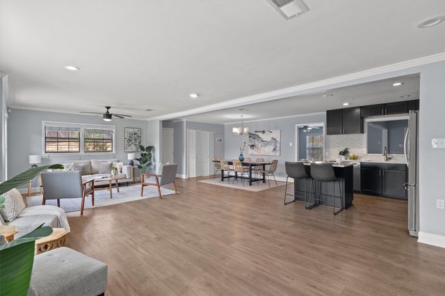 Living area featuring a healthy amount of sunlight, visible vents, light wood finished floors, crown molding, and ceiling fan with notable chandelier | Image 7