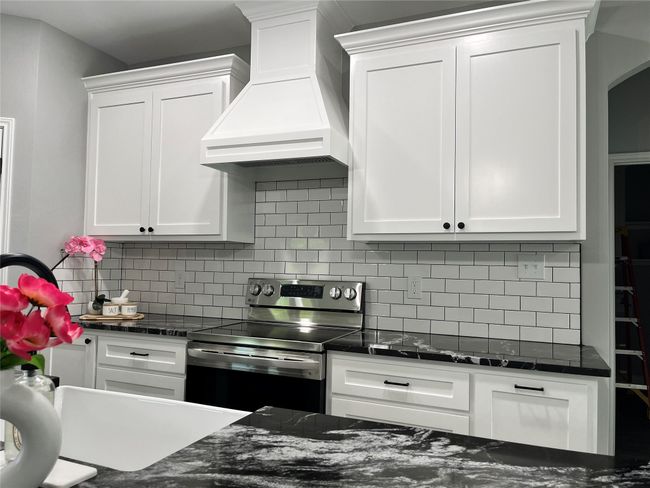 Kitchen featuring stainless steel electric range oven, custom exhaust hood, white cabinets, and backsplash | Image 9