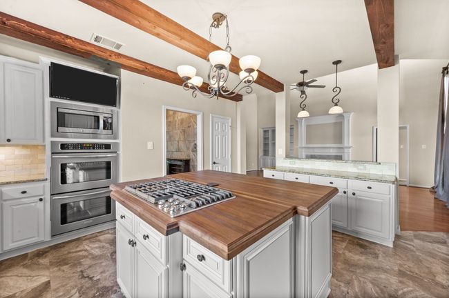 Kitchen with wooden counters, appliances with stainless steel finishes, beamed ceiling, tasteful backsplash, and a center island | Image 10