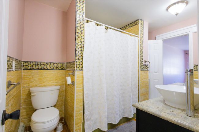 Bathroom featuring a baseboard heating unit, vanity, curtained shower, tile walls, and toilet | Image 16