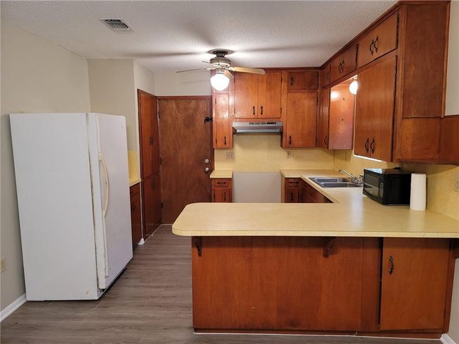 Kitchen featuring freestanding refrigerator, a peninsula, black microwave, brown cabinetry, and a ceiling fan | Image 7