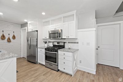 Kitchen with appliances with stainless steel finishes, white cabinetry, light wood-type flooring, and light stone counters | Image 3