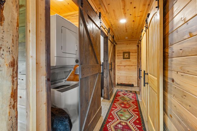 Laundry area with stacked washing machine and dryer, a barn door, wood walls, and wooden ceiling | Image 14