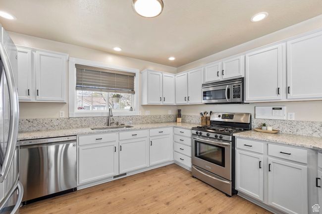 Kitchen featuring light wood-style floors, a sink, white cabinetry, and appliances with stainless steel finishes | Image 10