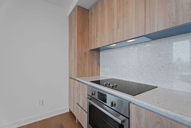 Kitchen with oven, modern cabinets, black electric stovetop, light brown cabinets, and backsplash | Image 7