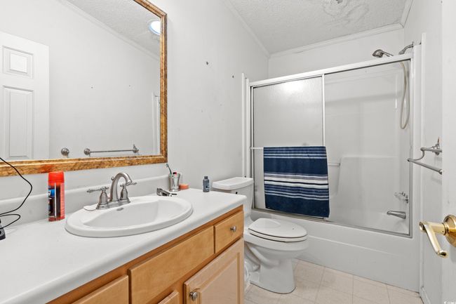 Bathroom with a textured ceiling, vanity, shower / bath combination with glass door, and ornamental molding | Image 23