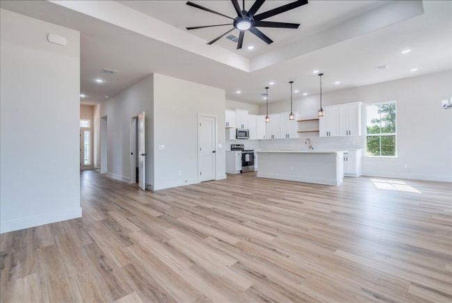 Unfurnished living room with ceiling fan, light wood-style floors, recessed lighting, and a raised ceiling | Image 6