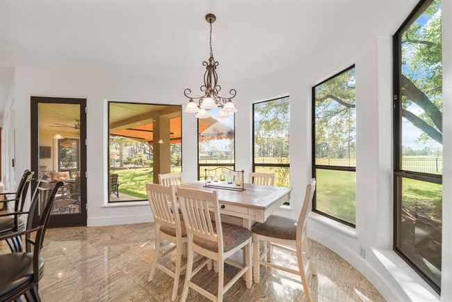 Bright & cheery and surrounded by windows overlooking the backyard, the breakfast room has a high ceiling with chandelier lighting, a glass door leading to the covered patio & tile flooring. | Image 17