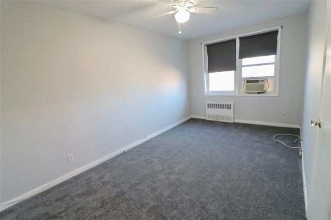Empty room with radiator heating unit, a ceiling fan, dark colored carpet, and cooling unit | Image 10
