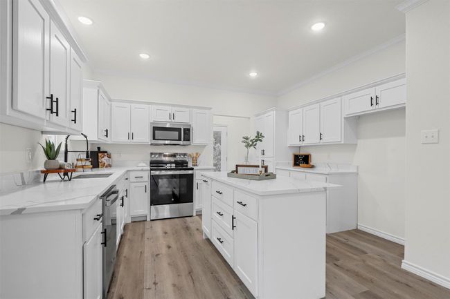 Kitchen with stainless steel appliances, light stone countertops, a center island, sink, and white cabinetry | Image 16