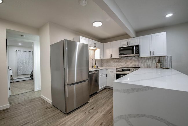 Kitchen with a baseboard heating unit, light wood-style floors, light stone counters, white cabinets, and appliances with stainless steel finishes | Image 6