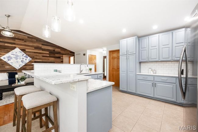 Kitchen featuring vaulted ceiling, gray cabinetry, wooden walls, tasteful backsplash, and freestanding refrigerator | Image 17