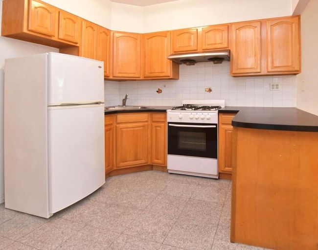 Kitchen featuring white appliances, under cabinet range hood, dark countertops, and granite tiled floors | Image 5
