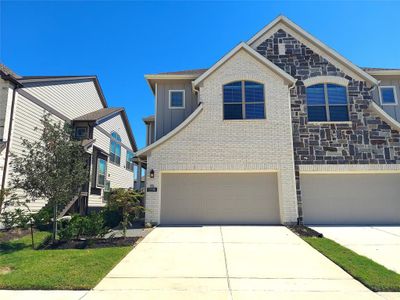 This is a modern two-story home featuring a mix of stone and siding exterior with a two-car garage and a well-maintained lawn, set under a clear blue sky. | Image 1