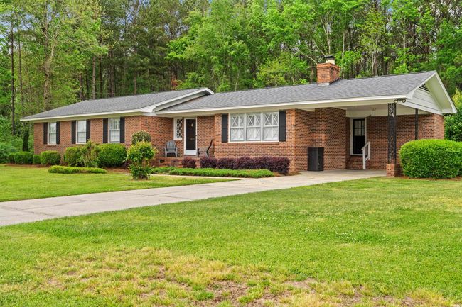 Ranch-style house with a front lawn, an attached carport, driveway, a chimney, and brick siding | Image 27
