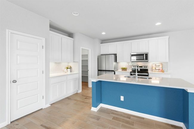 Kitchen with stainless steel appliances, tasteful backsplash, light countertops, light wood-type flooring, and white cabinets | Image 11