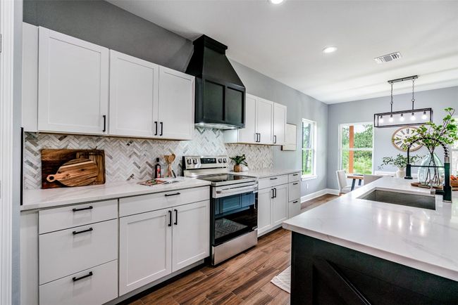 Kitchen with electric range, dark wood-style flooring, backsplash, a sink, and white cabinets | Image 9