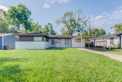 This is a single-story home with a carport, featuring a mix of brick and siding exterior, and a well-maintained lawn surrounded by mature trees. | Image 1